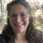 A picture of Jayne McBurney, a woman with shoulder-length curly hair and glasses, smiling at the camera.